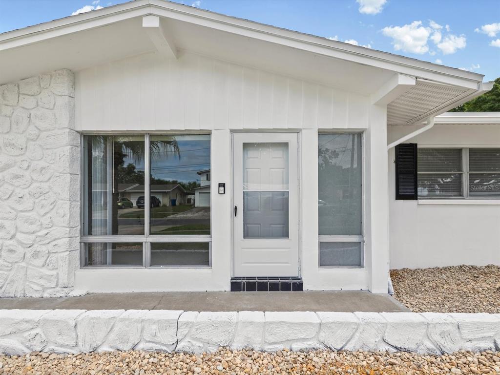 The exterior of a white house features a stone-textured wall, a glass door, and windows — 865 IMPERIAL DRIVE, LARGO, FL