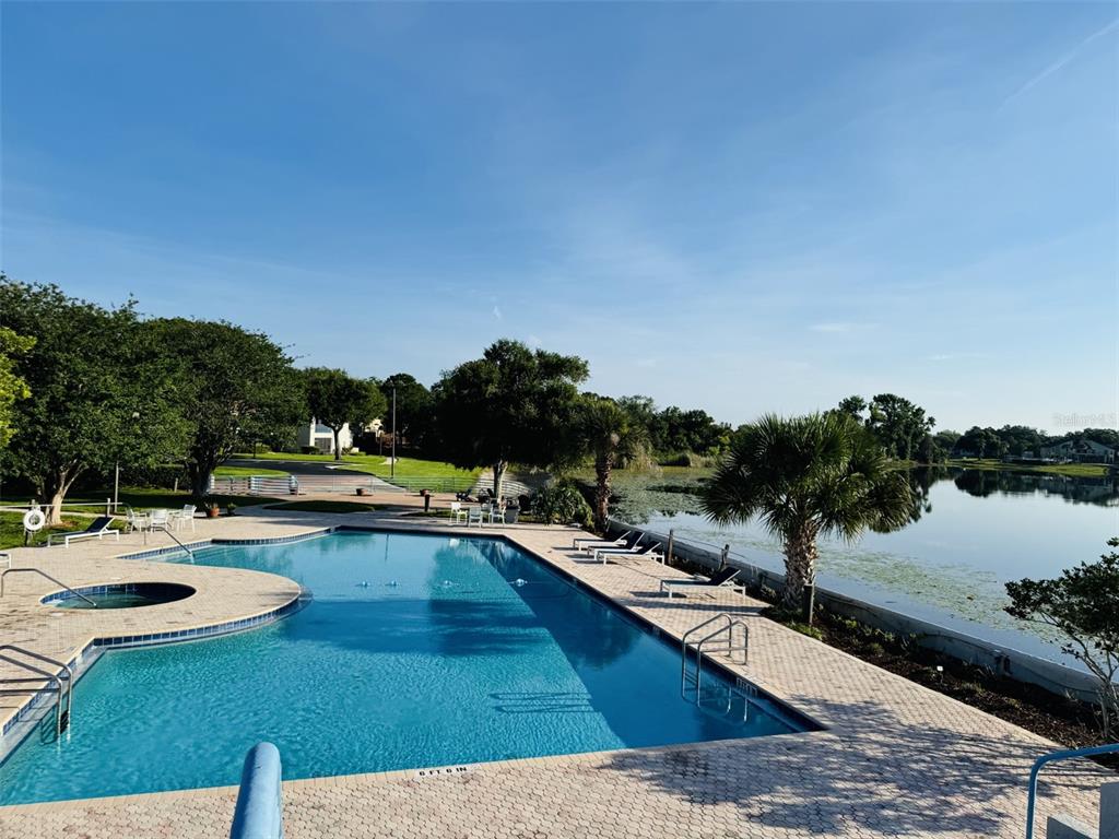 Two dark blue Adirondack chairs sit on a grassy lawn overlooking a calm lake — 1000 WINDERLEY PLACE UNIT 128, MAITLAND, FL