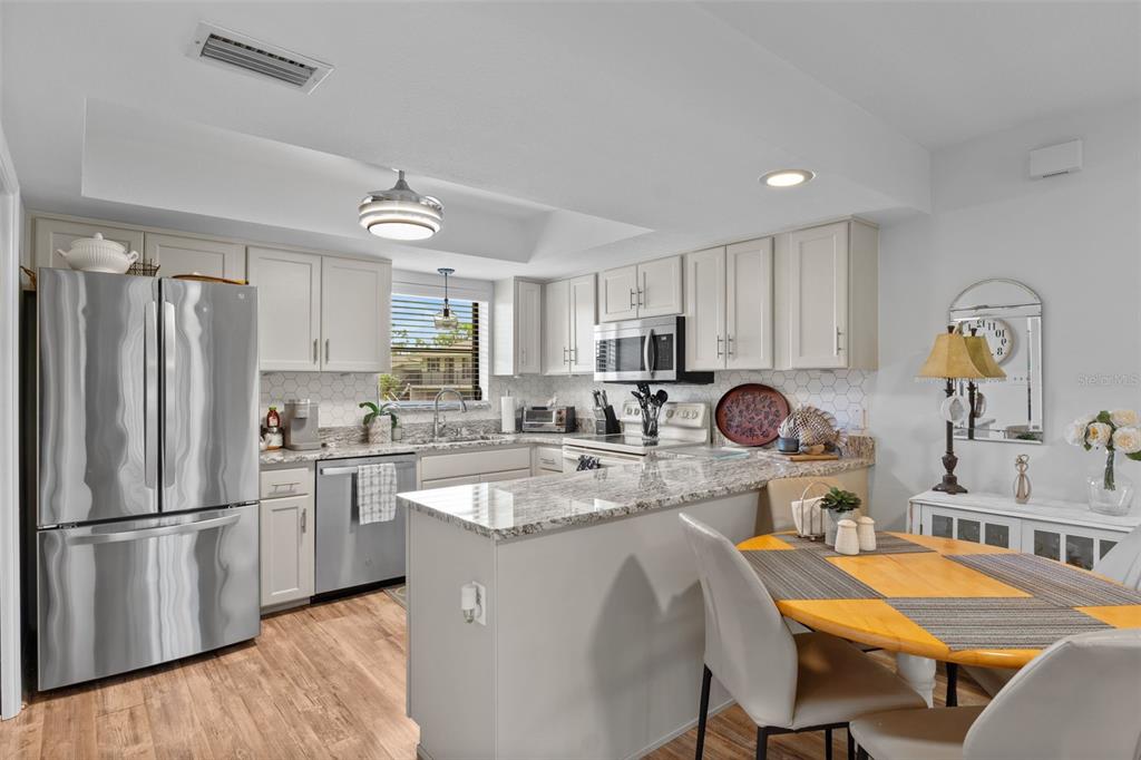 A kitchen with light-colored cabinets, granite countertops, stainless steel appliances, and an adjacent dining area — 4260 PLACIDA ROAD UNIT 17A, ENGLEWOOD, FL