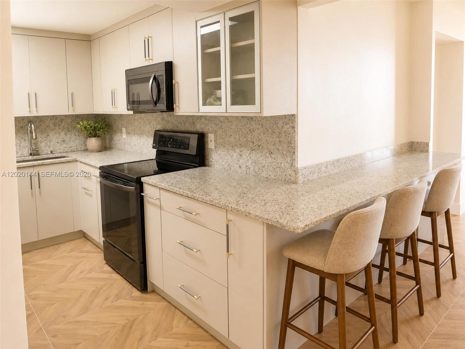 A kitchen features light-colored cabinets, speckled countertops, black appliances, and a breakfast bar with stools — 2500 Parkview Dr # 1816, Hallandale Beach FL 33009, HALLANDALE BEACH, FL