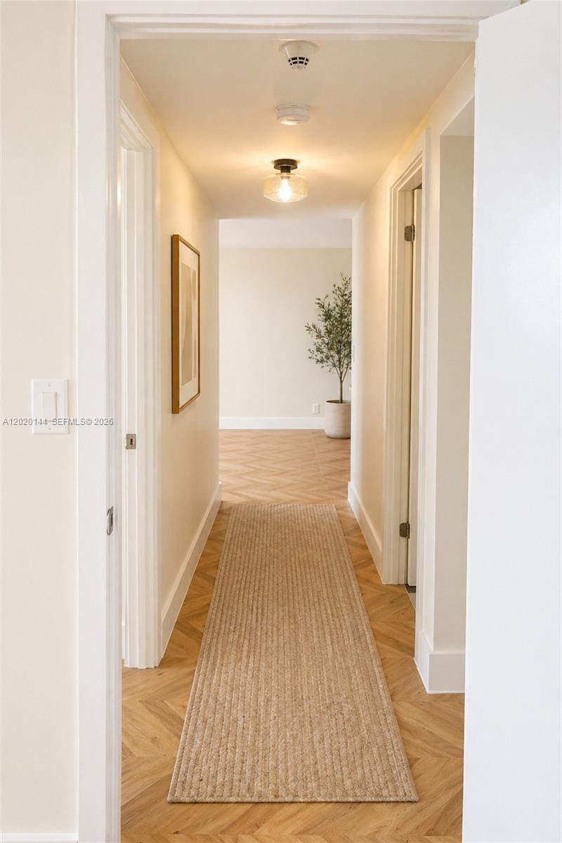 A hallway with herringbone wood floors leads to an open room with a potted plant — 2500 Parkview Dr # 1816, Hallandale Beach FL 33009, HALLANDALE BEACH, FL