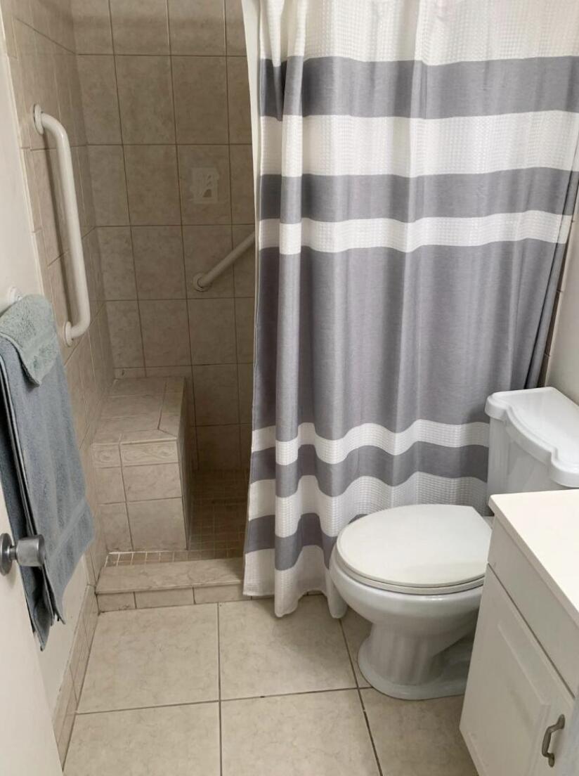 A bathroom features a tiled walk-in shower with a built-in bench and grab bars — 74 Sheffield D, West Palm Beach FL 33417, WEST PALM BEACH, FL