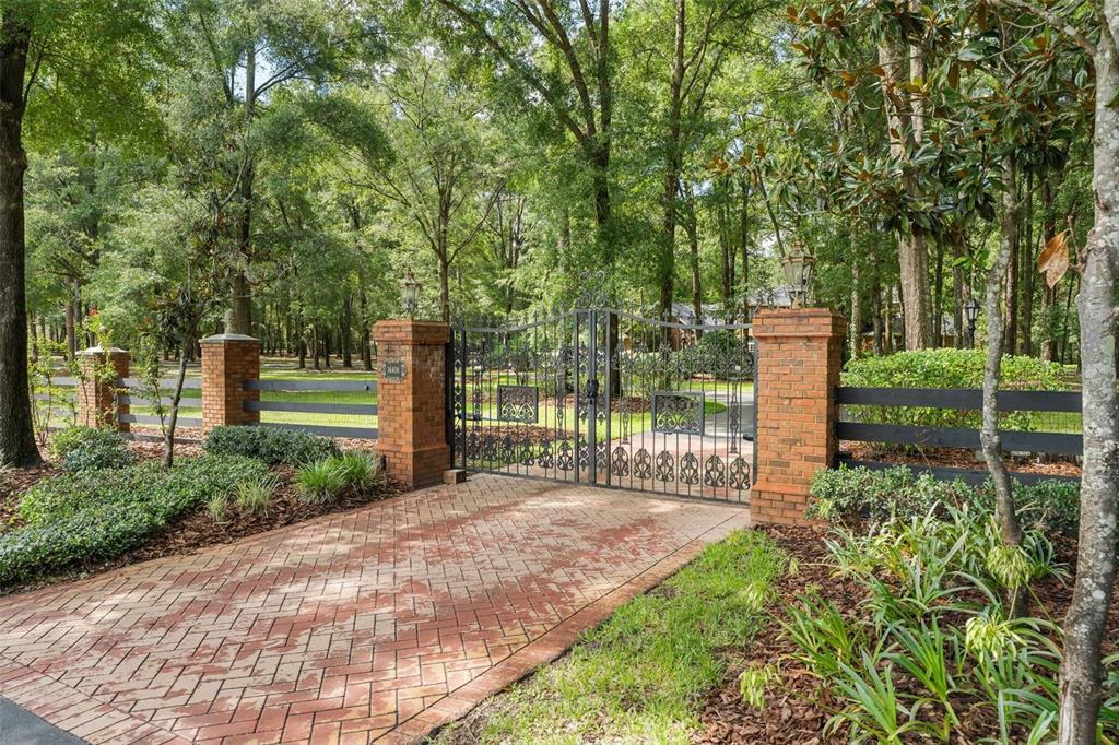 A brick-paved driveway leads to a black metal gate flanked by brick pillars and fencing — 14408 NW 50TH PLACE, ALACHUA, FL