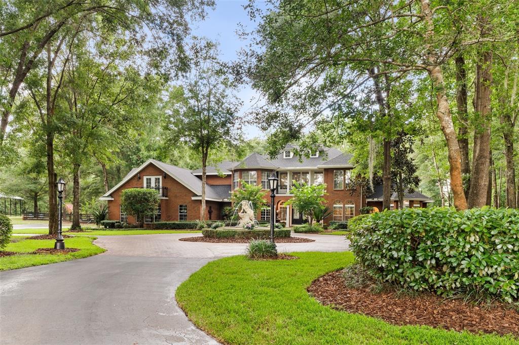 A large two-story brick house features a circular driveway with a central fountain and landscaping — 14408 NW 50TH PLACE, ALACHUA, FL