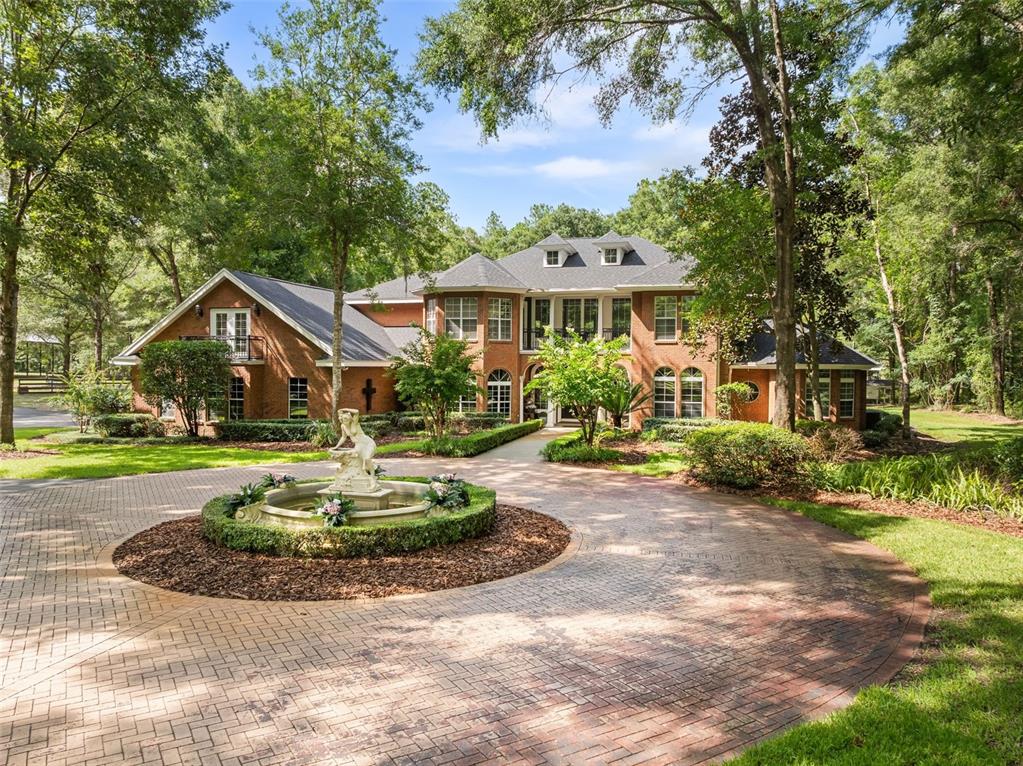 A large brick house with a circular driveway and a central fountain in the front yard — 14408 NW 50TH PLACE, ALACHUA, FL