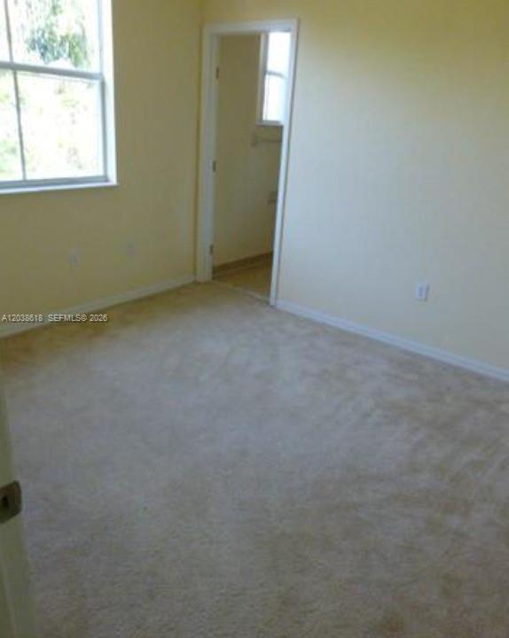 A carpeted bedroom with light yellow walls, a window, and a doorway leading to another room — 641 E Mowry Ct, Homestead FL 33030, HOMESTEAD, FL