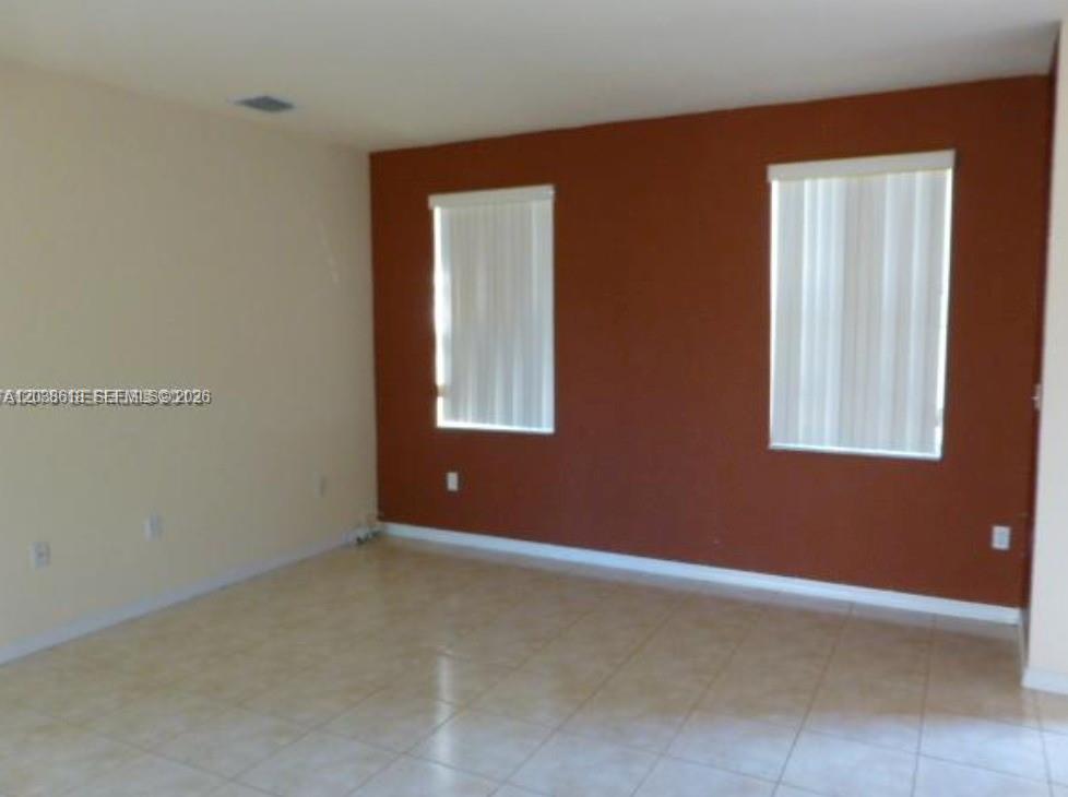 An empty room features beige tile flooring, light-colored walls, and a single rust-colored accent wall — 641 E Mowry Ct, Homestead FL 33030, HOMESTEAD, FL