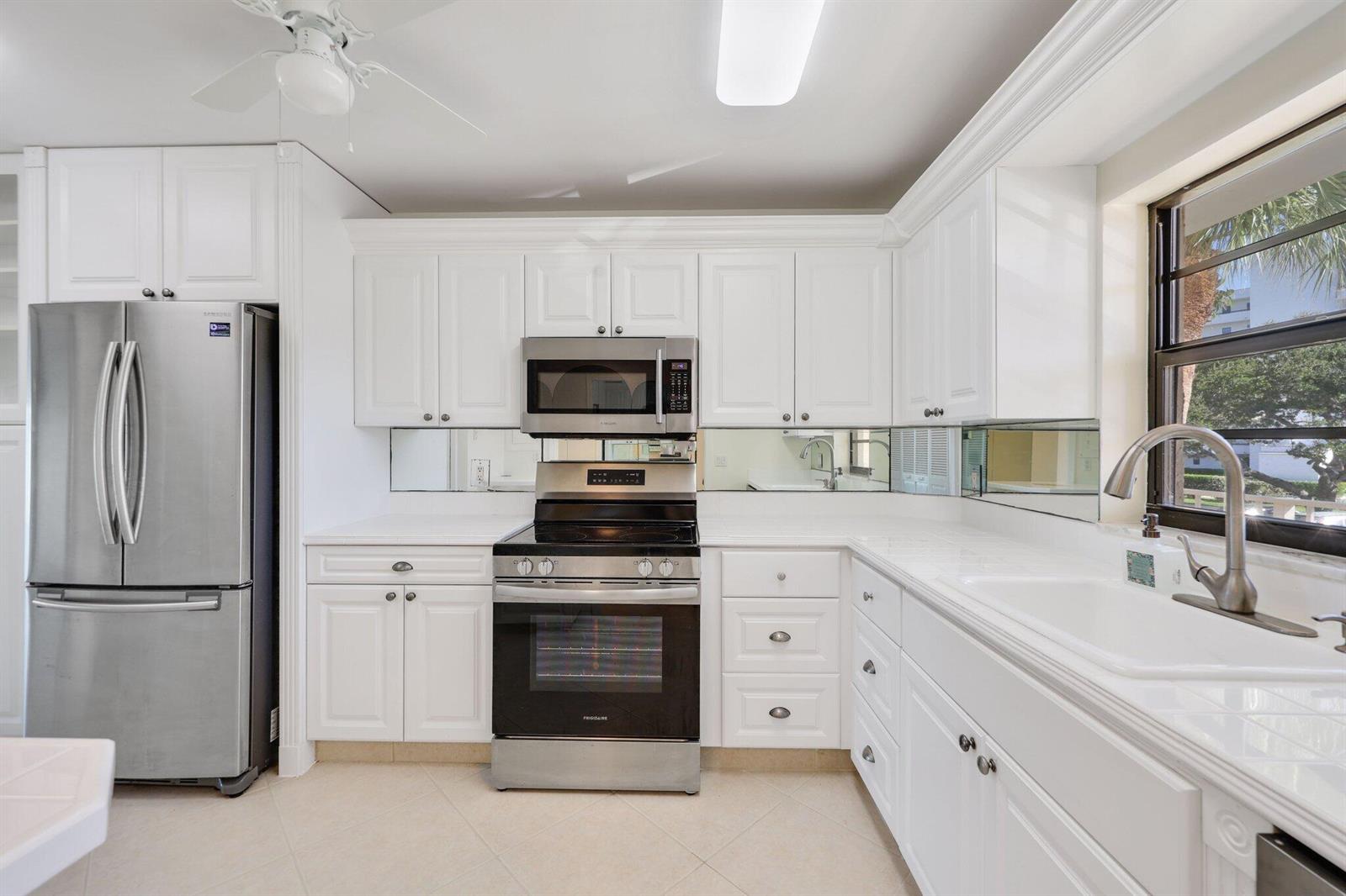 A kitchen with white cabinets, stainless steel appliances, a mirrored backsplash, and tile flooring — 200 Intracoastal Place # 206, Jupiter FL 33469, JUPITER, FL
