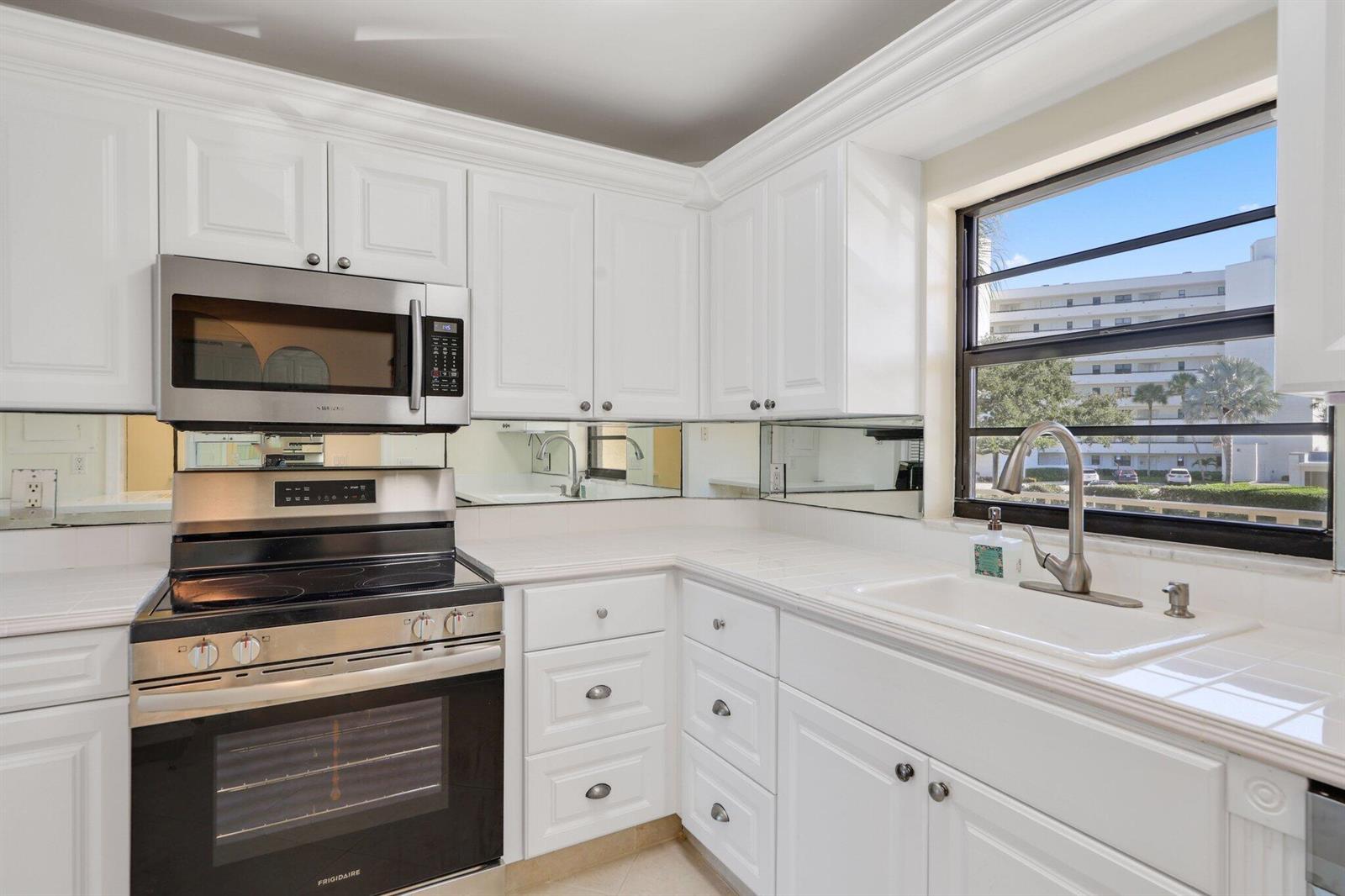 A kitchen features white cabinets, stainless steel appliances, a tiled countertop, and a mirrored backsplash — 200 Intracoastal Place # 206, Jupiter FL 33469, JUPITER, FL