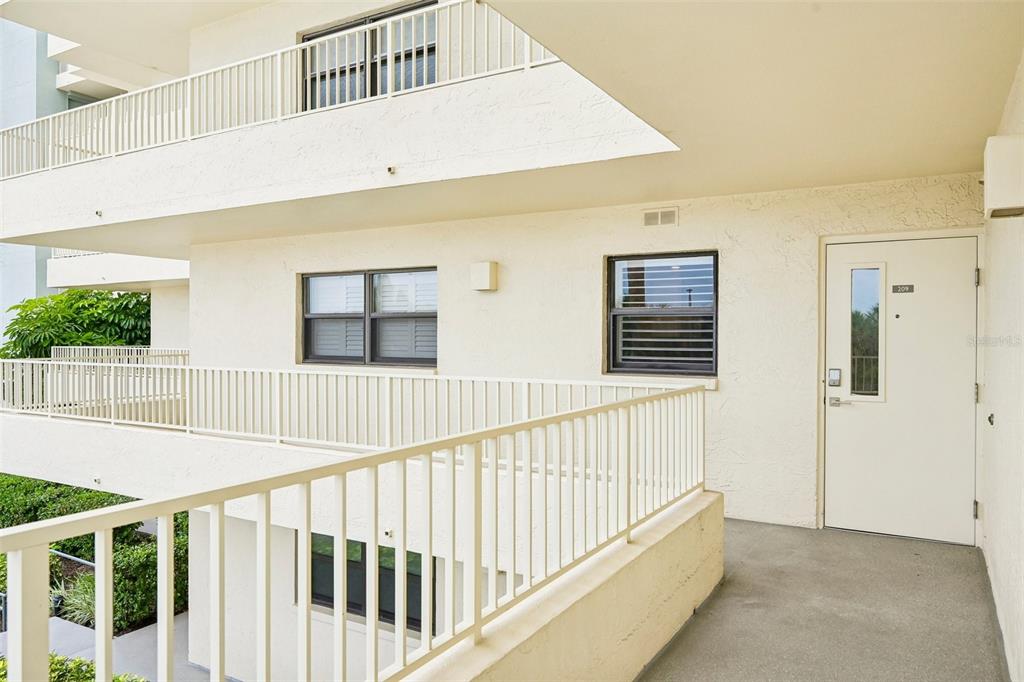 An exterior view of a second-floor apartment balcony with a white door and railings — 5760 MIDNIGHT PASS ROAD UNIT #209D, SARASOTA, FL