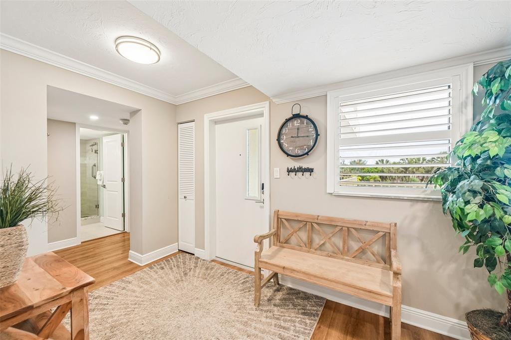A bright entryway features a wooden bench, a wall clock, and a window with shutters — 5760 MIDNIGHT PASS ROAD UNIT #209D, SARASOTA, FL