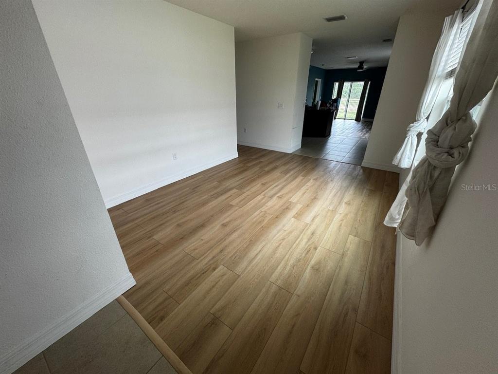 An empty room with light wood-look flooring leads to a kitchen area with tiled floors — 10526 WHISPERING HAMMOCK DRIVE, RIVERVIEW, FL