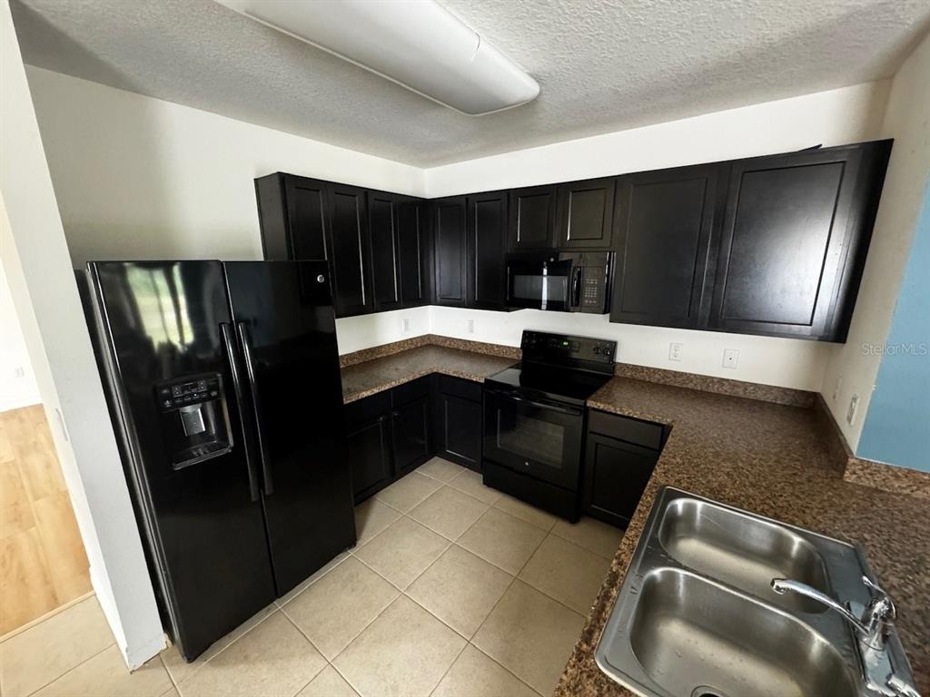 A kitchen features black cabinets, black appliances, brown countertops, and light-colored tile flooring — 10526 WHISPERING HAMMOCK DRIVE, RIVERVIEW, FL