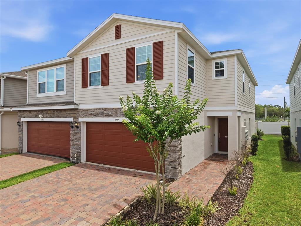A two-story townhouse with tan siding, stone veneer, and two brown garage doors — 1255 WISPY CYPRESS DRIVE, KISSIMMEE, FL