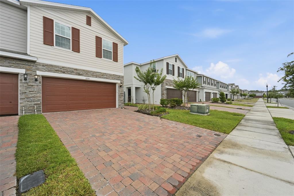 A row of two-story townhomes with brick paver driveways and attached garages under a blue sky — 1255 WISPY CYPRESS DRIVE, KISSIMMEE, FL
