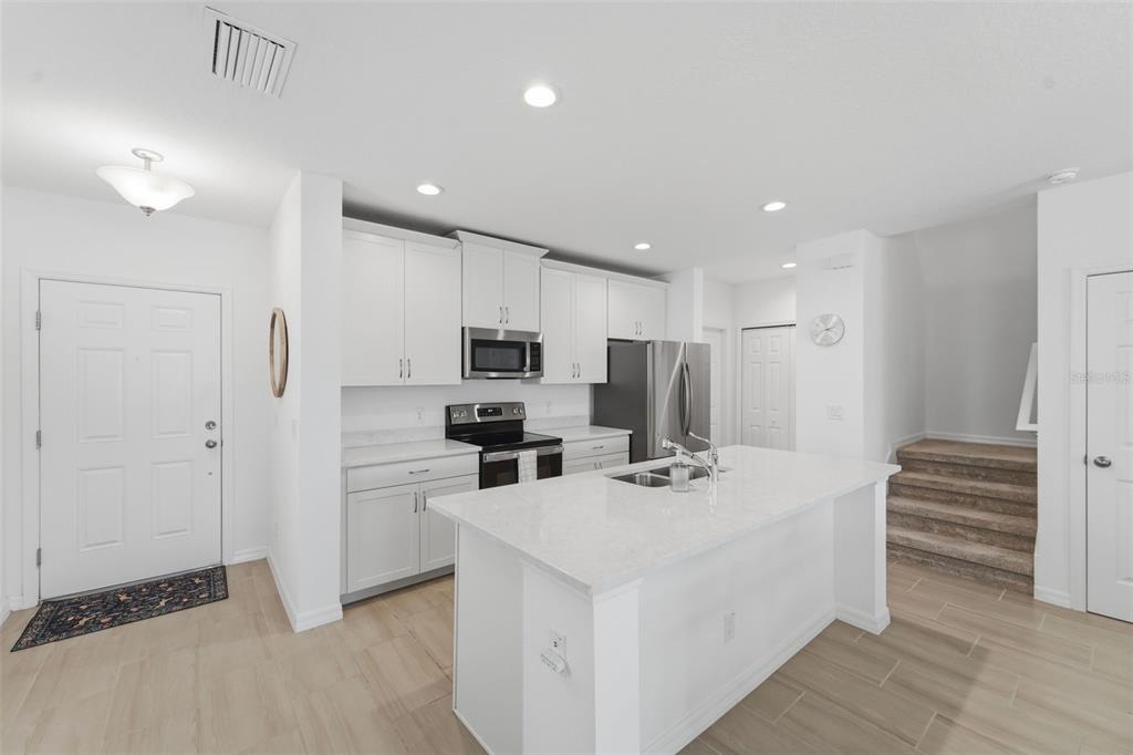 A modern kitchen features white cabinetry, a central island with a sink, and light flooring — 1255 WISPY CYPRESS DRIVE, KISSIMMEE, FL