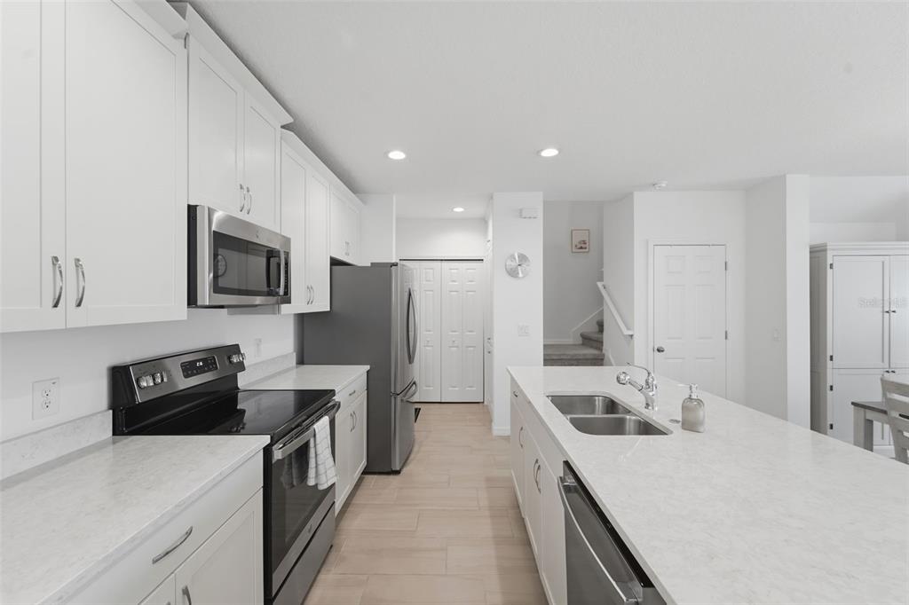 A modern kitchen features white cabinets, stainless steel appliances, and a large quartz-topped island — 1255 WISPY CYPRESS DRIVE, KISSIMMEE, FL