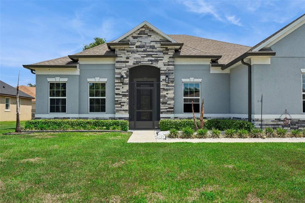 A single-story house with a gray stucco exterior, stone facade accents, and a screened entryway — 714 OAKS SHORES ROAD, LEESBURG, FL
