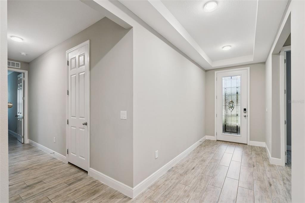 A bright entryway features light wood-look tile flooring, gray walls, and a glass-paneled front door — 714 OAKS SHORES ROAD, LEESBURG, FL