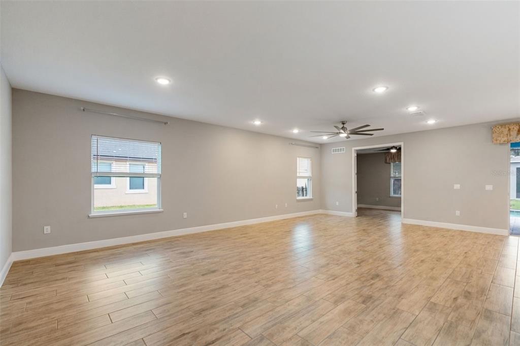A spacious, empty living room features light gray walls, wood-look tile flooring, and recessed lighting — 714 OAKS SHORES ROAD, LEESBURG, FL
