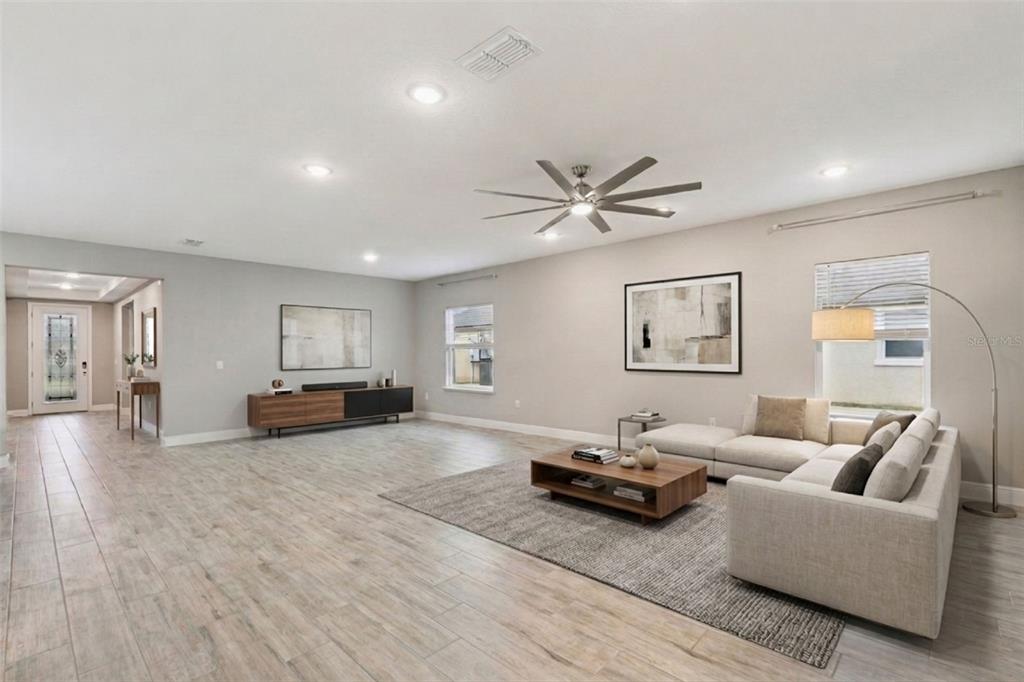 A spacious living room features light wood-look tile flooring, a sectional sofa, and recessed lighting — 714 OAKS SHORES ROAD, LEESBURG, FL