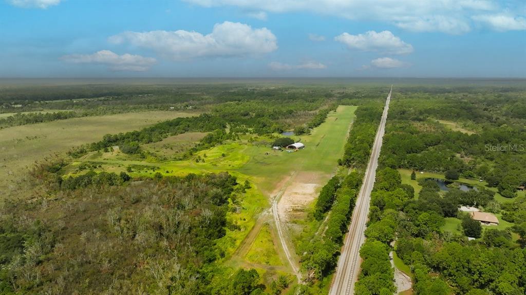An aerial view shows a rural property with a grass airstrip, hangar, and railroad tracks — 520 HIGHLANDER DRIVE Lot 1, OAK HILL, FL