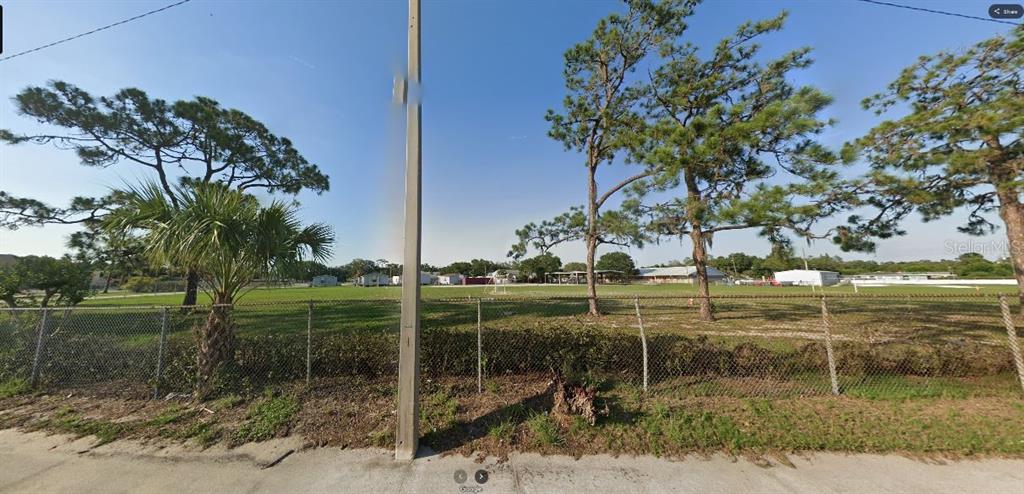 A chain-link fence borders a flat, grassy vacant lot with several pine trees and palms — HWY 60 E, LAKE WALES, FL
