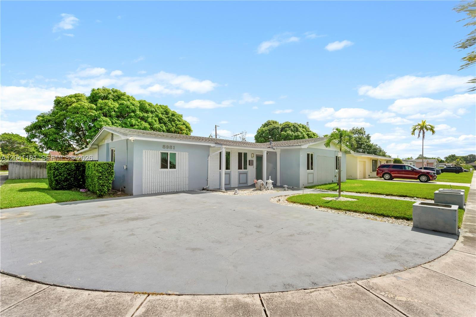 A light blue single-story house features a large concrete driveway and a manicured lawn — 8981 SW 127th Ter, Miami FL 33176, MIAMI, FL