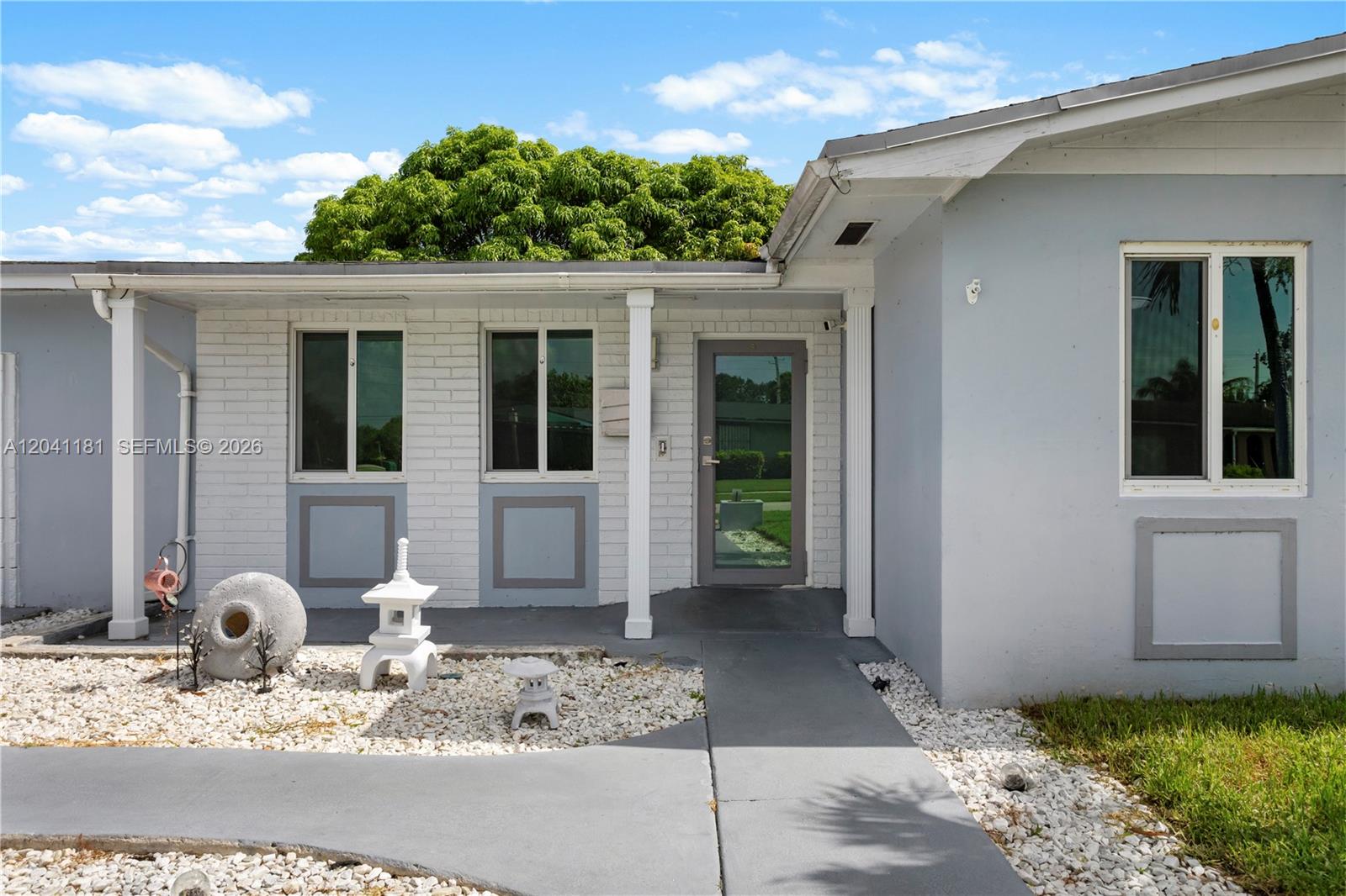 The exterior of a house features a white brick facade, grey trim, and a stone garden — 8981 SW 127th Ter, Miami FL 33176, MIAMI, FL
