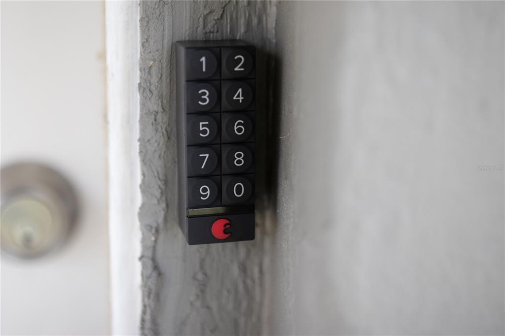 A black August smart keypad is mounted on a textured gray wall next to a door — 123 OCONEE STREET, LAKELAND, FL