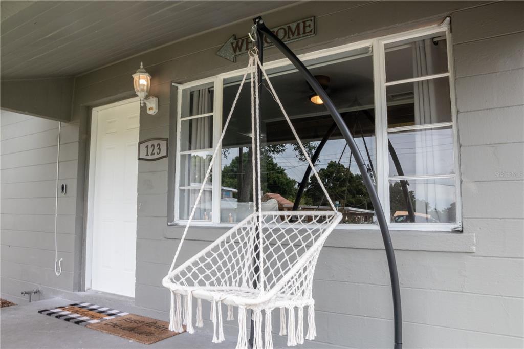 A white macrame hanging chair sits on a gray porch in front of a house entrance — 123 OCONEE STREET, LAKELAND, FL