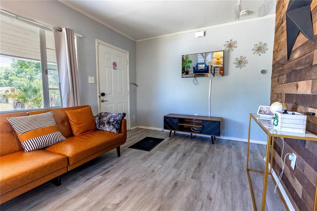 A living room features a brown leather sofa, wood-paneled accent wall, and light wood flooring — 123 OCONEE STREET, LAKELAND, FL