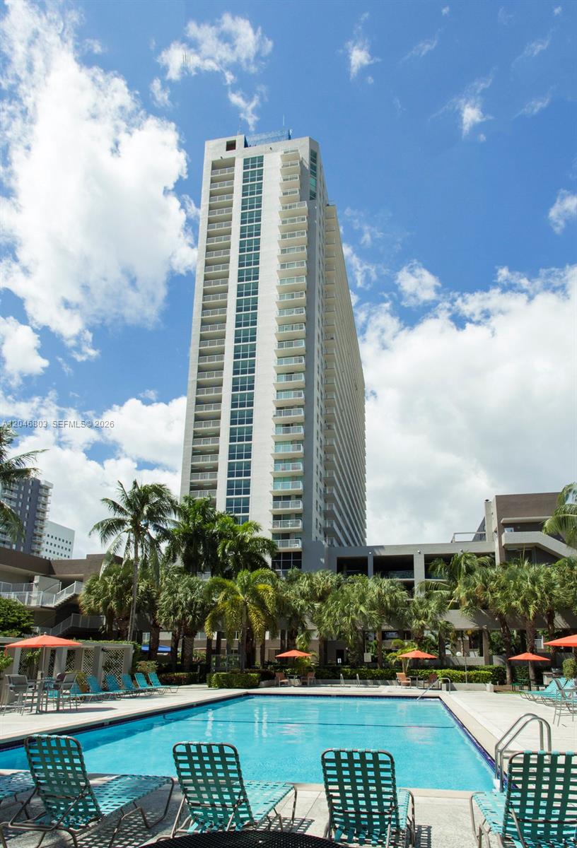 A tall residential high-rise building stands behind a swimming pool with lounge chairs — 915 NW 1st Ave # H2208, Miami FL 33136, MIAMI, FL