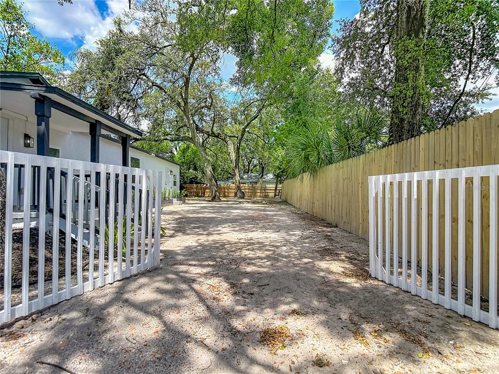 A sandy driveway leads between a white picket fence and a tall wooden privacy fence — 10009 N FLORENCE AVENUE, TAMPA, FL