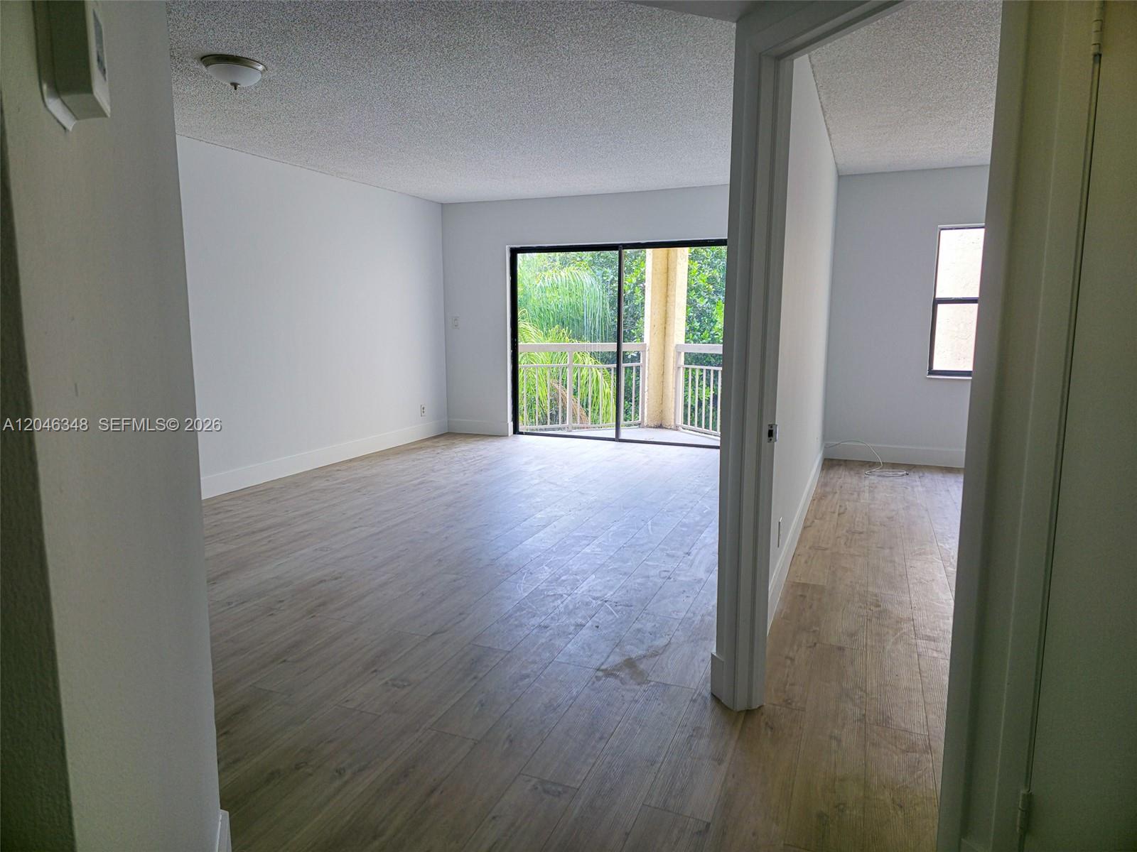 An empty room with light wood-look flooring, white walls, and a sliding glass door balcony — 8290 Lake Dr # 422, Doral FL 33166, DORAL, FL