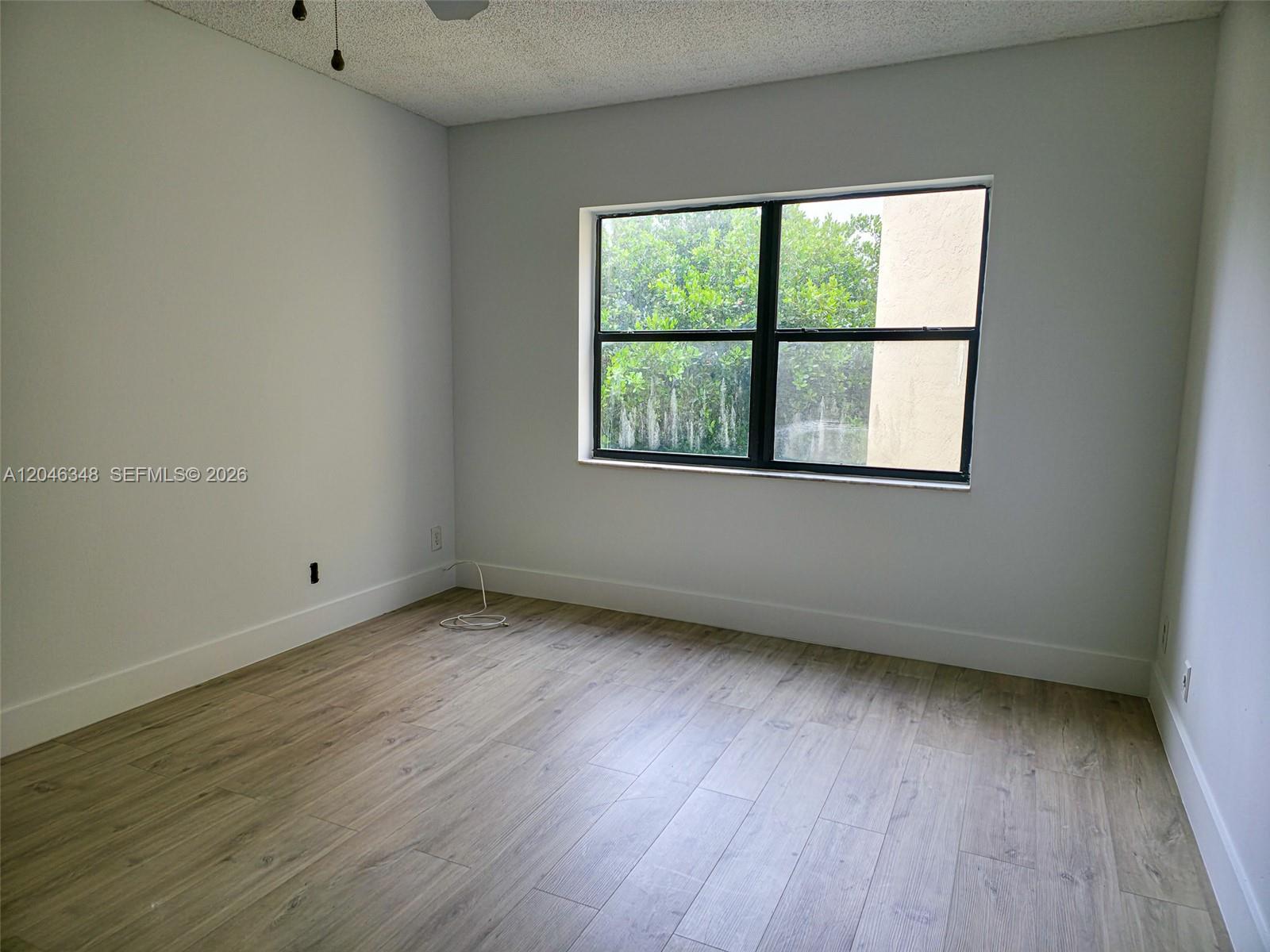 An empty room features light gray walls, wood-look flooring, and a window overlooking greenery — 8290 Lake Dr # 422, Doral FL 33166, DORAL, FL