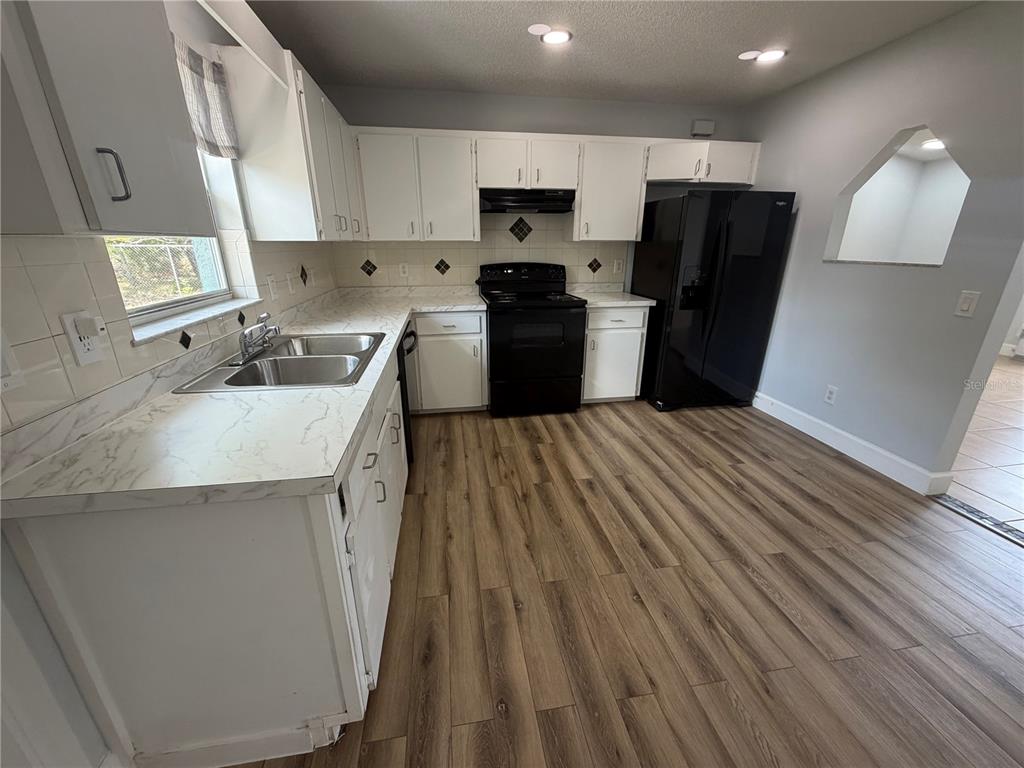 A kitchen features white cabinets, marble-look countertops, black appliances, and wood-look flooring — 36 PECAN RUN COURSE, OCALA, FL