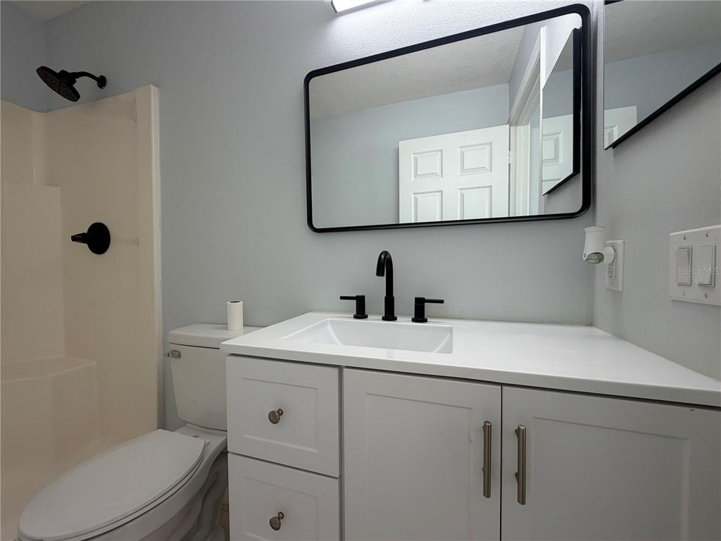 A bathroom features a white vanity with a black faucet, a mirror, and a shower — 36 PECAN RUN COURSE, OCALA, FL