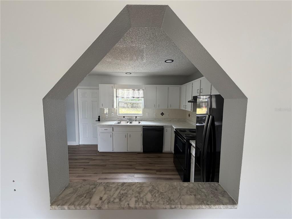 A view through a hexagonal opening into a kitchen with white cabinets and appliances — 36 PECAN RUN COURSE, OCALA, FL
