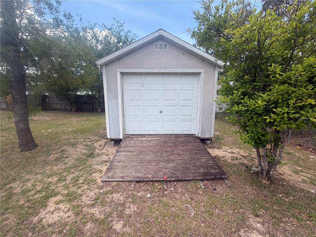A detached shed with a white garage door and a wooden ramp in a yard — 36 PECAN RUN COURSE, OCALA, FL
