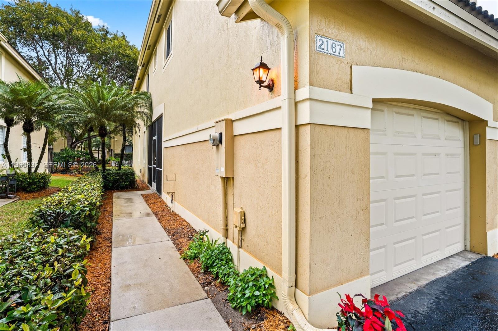 A side view of a tan stucco building exterior featuring a garage and a walkway — 2167 Hacienda Ter, Weston FL 33327, WESTON, FL