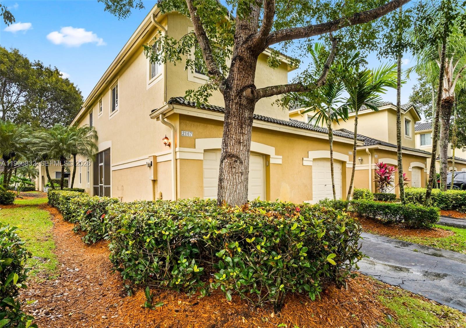 A two-story tan townhouse with a garage, a large tree, and manicured hedges in front — 2167 Hacienda Ter, Weston FL 33327, WESTON, FL