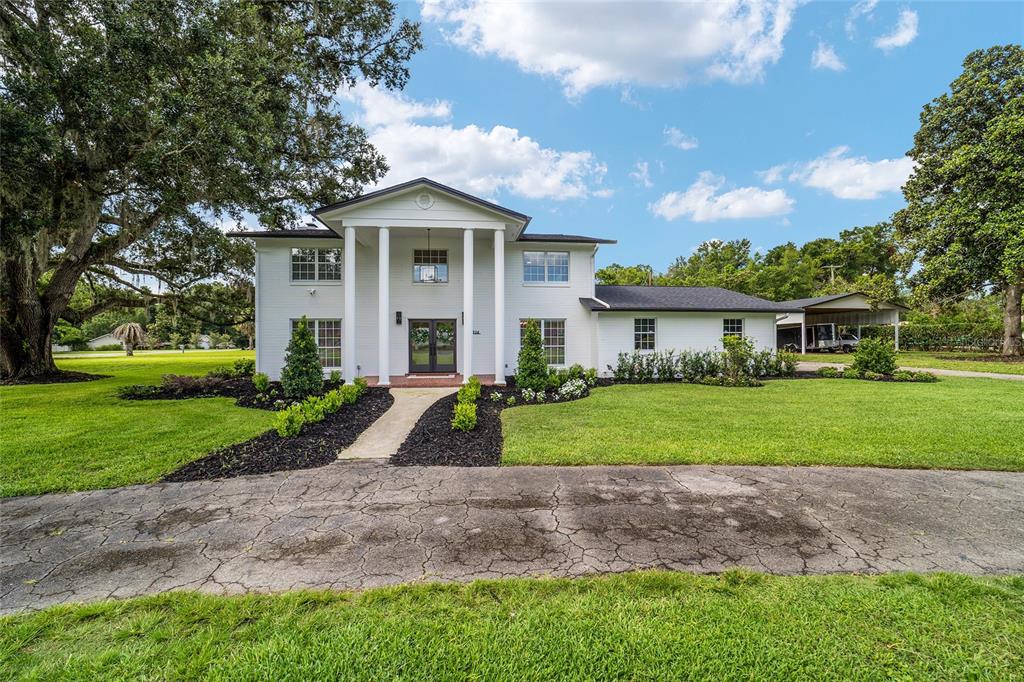 A two-story white house with a columned portico stands behind a cracked concrete driveway — 4824 SE 3RD STREET, OCALA, FL