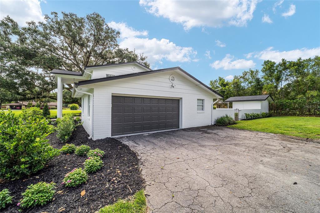A white brick house with a dark garage door and a cracked asphalt driveway — 4824 SE 3RD STREET, OCALA, FL
