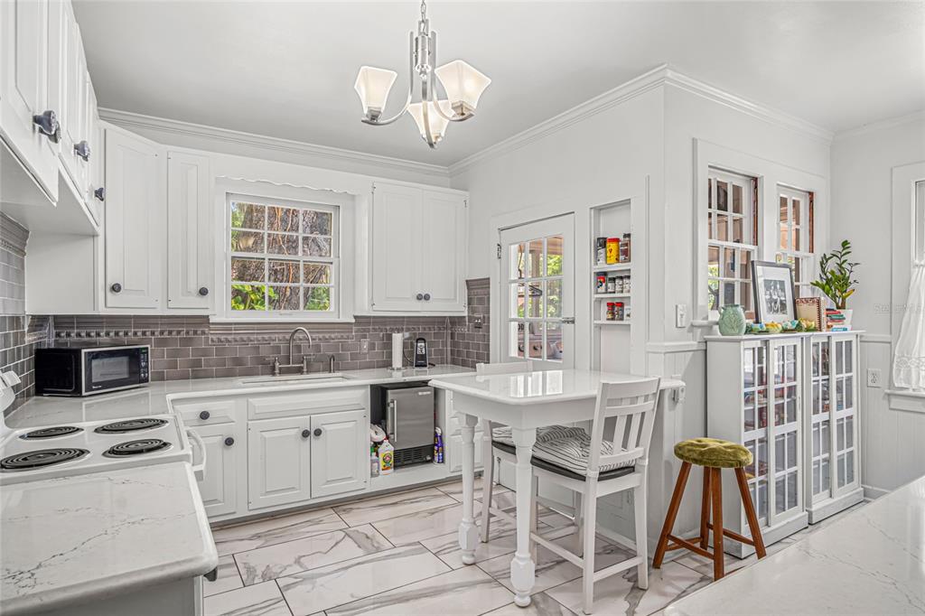 A white kitchen features marble-look tile floors, gray subway tile backsplash, and a small dining table — 102 PALMORA BOULEVARD, LEESBURG, FL