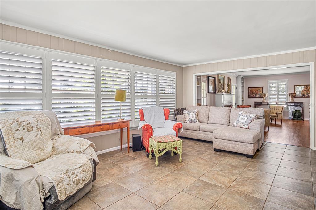 A living room features tile flooring, a beige sectional sofa, and large windows with shutters — 102 PALMORA BOULEVARD, LEESBURG, FL