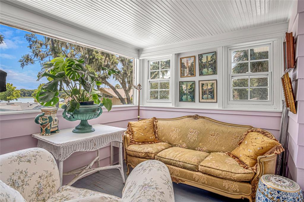 A sunroom features a gold sofa, a white wicker table, and windows overlooking a lake — 102 PALMORA BOULEVARD, LEESBURG, FL