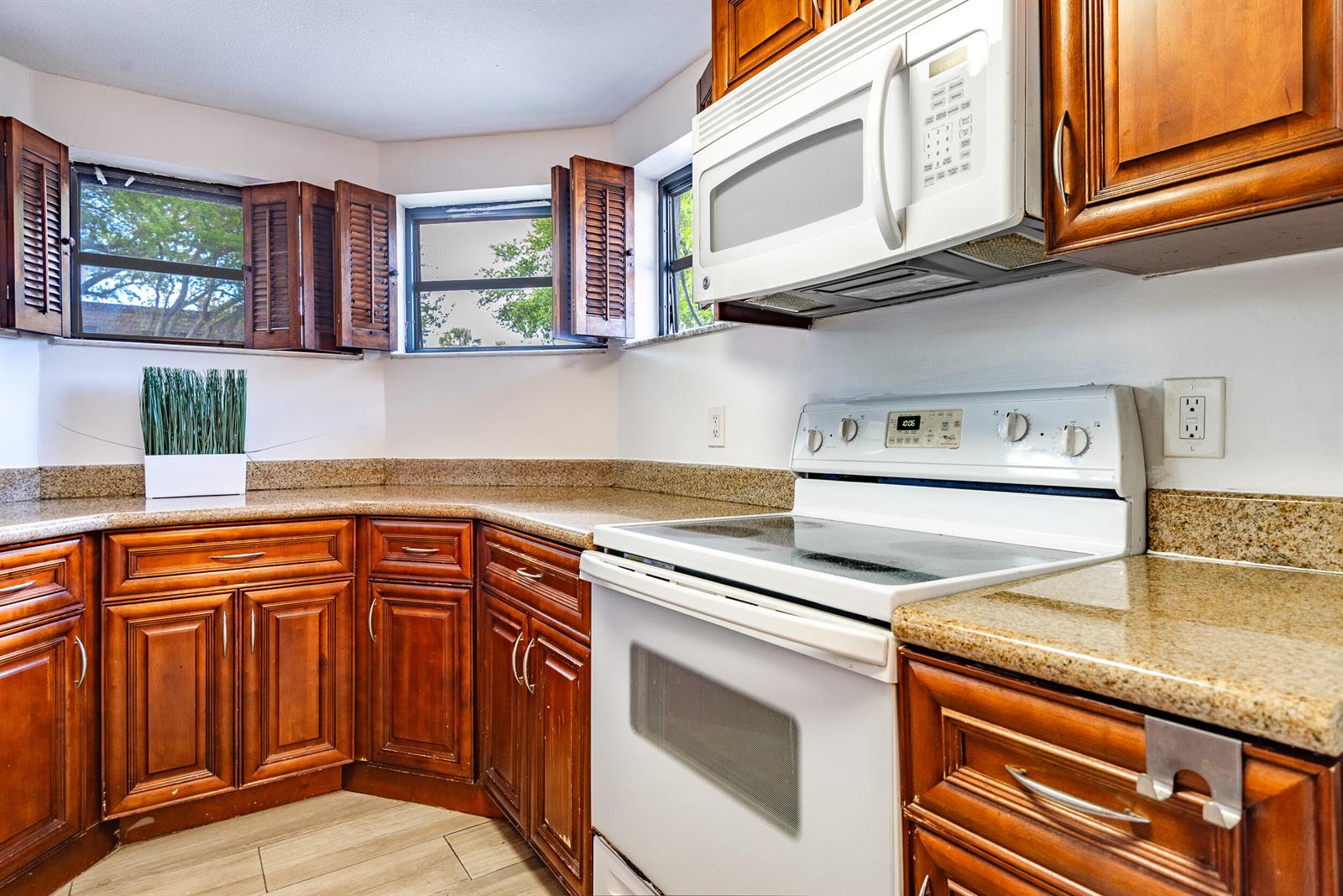 A kitchen features wood cabinets, granite countertops, a white stove, and a microwave — 9375 SW 61st Way SW # D, Boca Raton FL 33428, BOCA RATON, FL