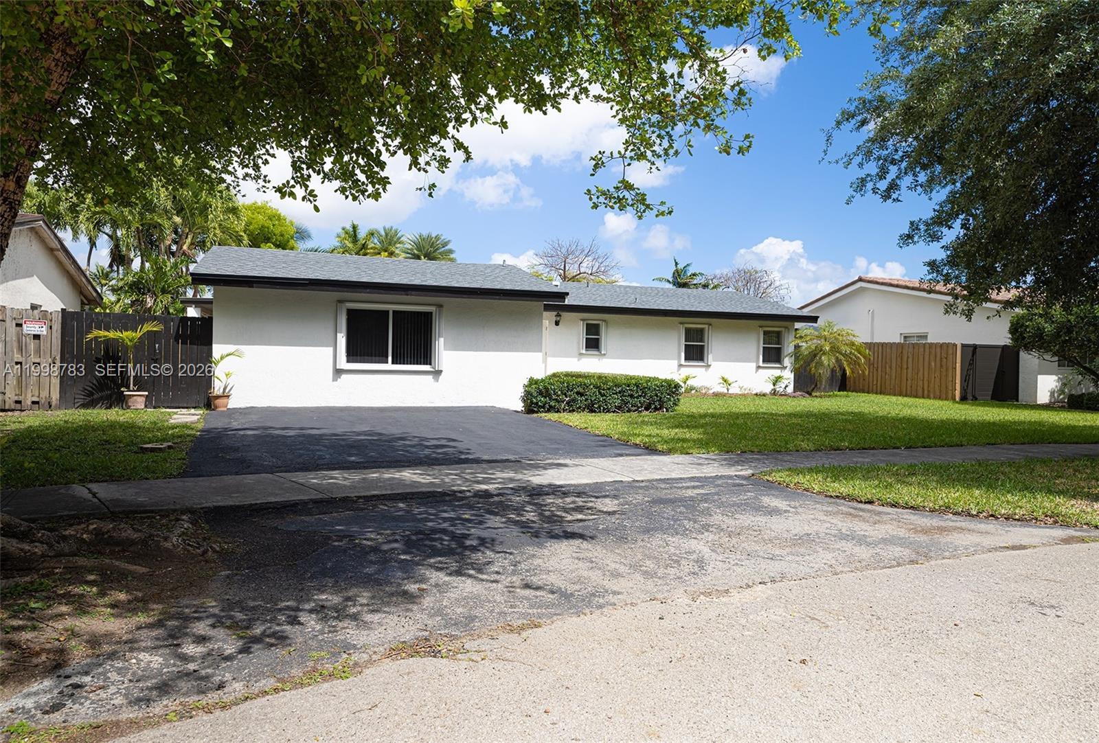 A single-story white house with a dark roof and asphalt driveway sits under a tree — 10241 SW 128th Ave, Miami FL 33186, MIAMI, FL