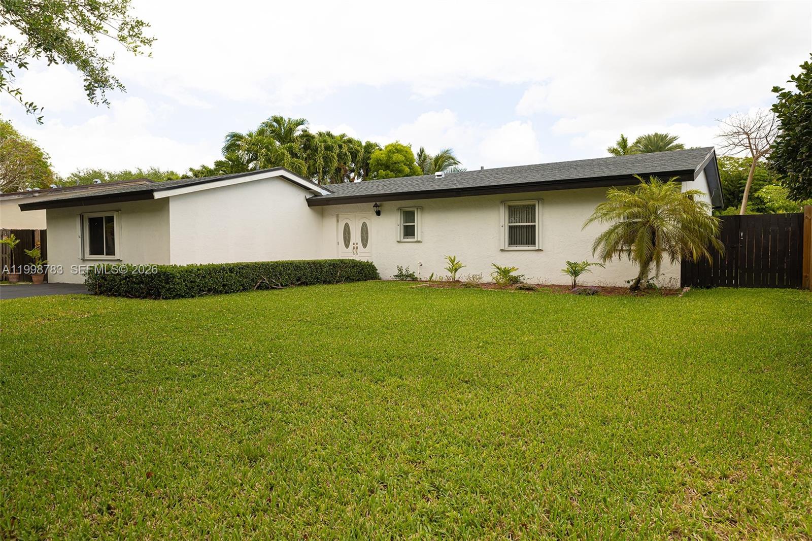A white, single-story house with a dark roof sits behind a large green lawn — 10241 SW 128th Ave, Miami FL 33186, MIAMI, FL